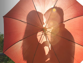 couple kissing behind red umbrella